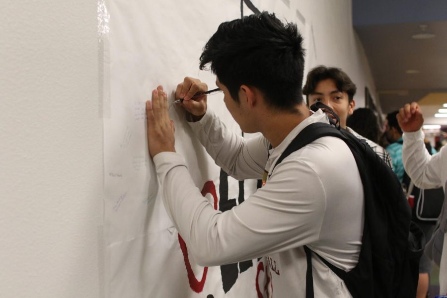 Senior Angel Espinoza writes a message on the memorial banner in the cafeteria on the second anniversary of the Wal-Mart mass shooting. 
